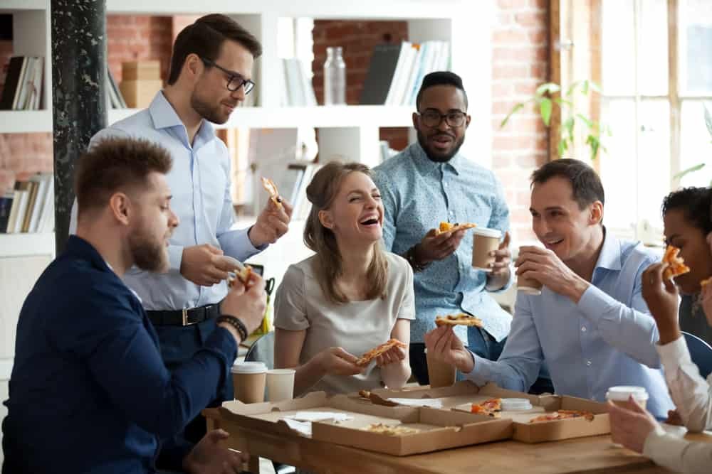 Co-workers talking and laughing while eating pizza at office 1