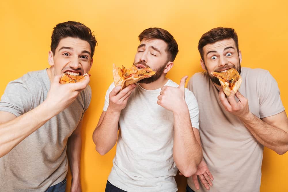 Three guys eating pizza isolated over yellow background